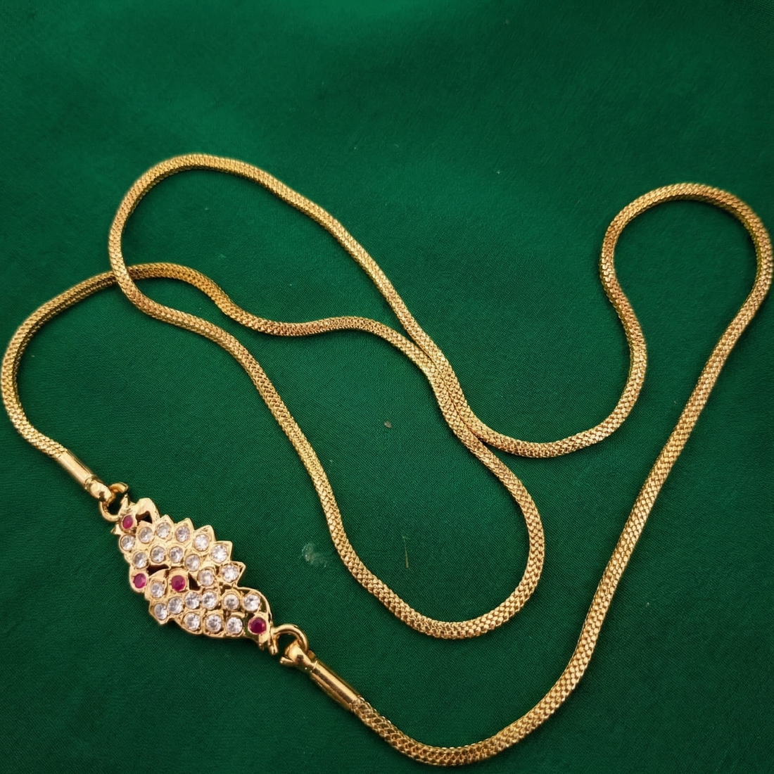 Gold necklace with a decorative pendant on a green background