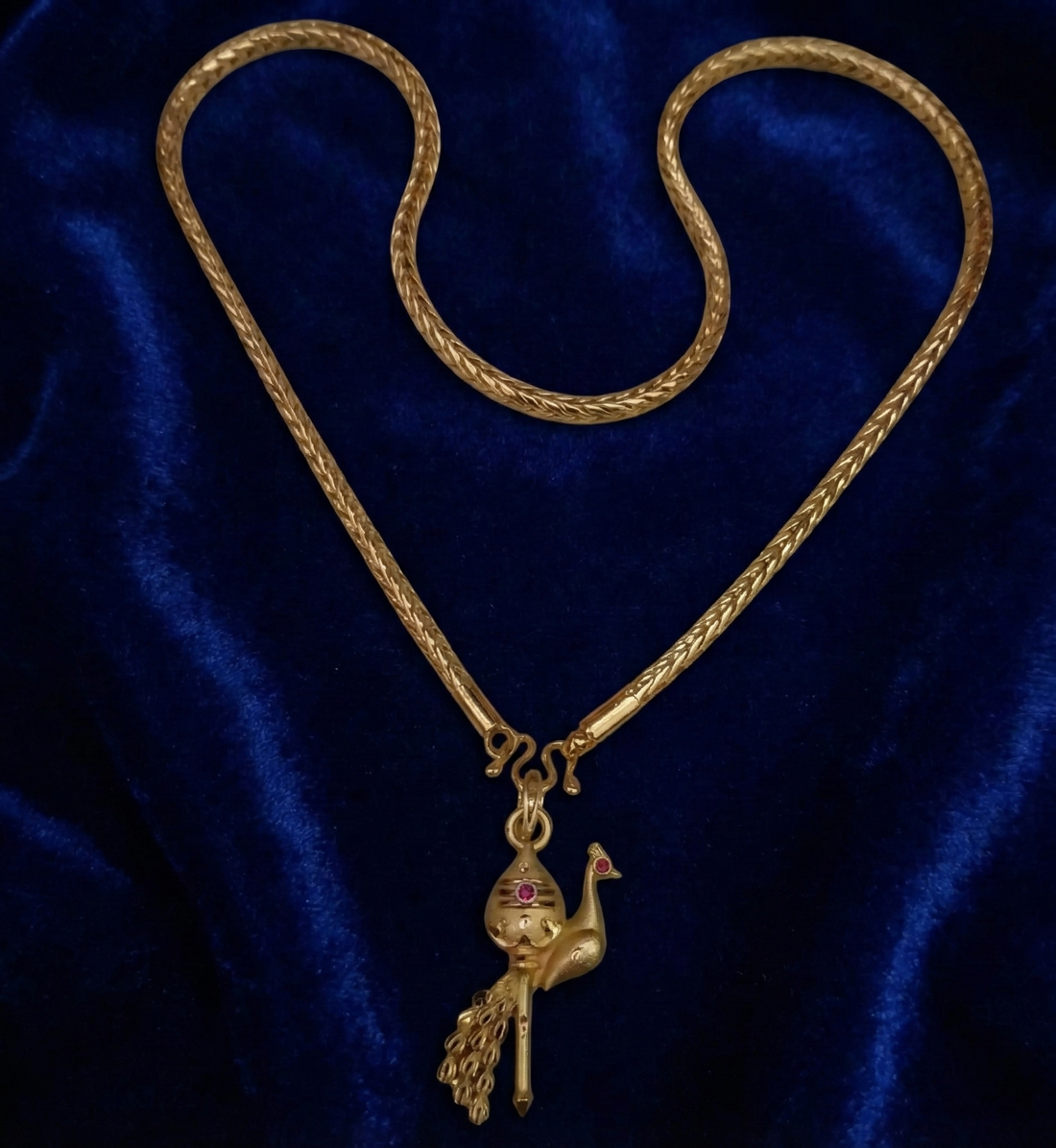 Gold necklace with a peacock pendant on a blue velvet background