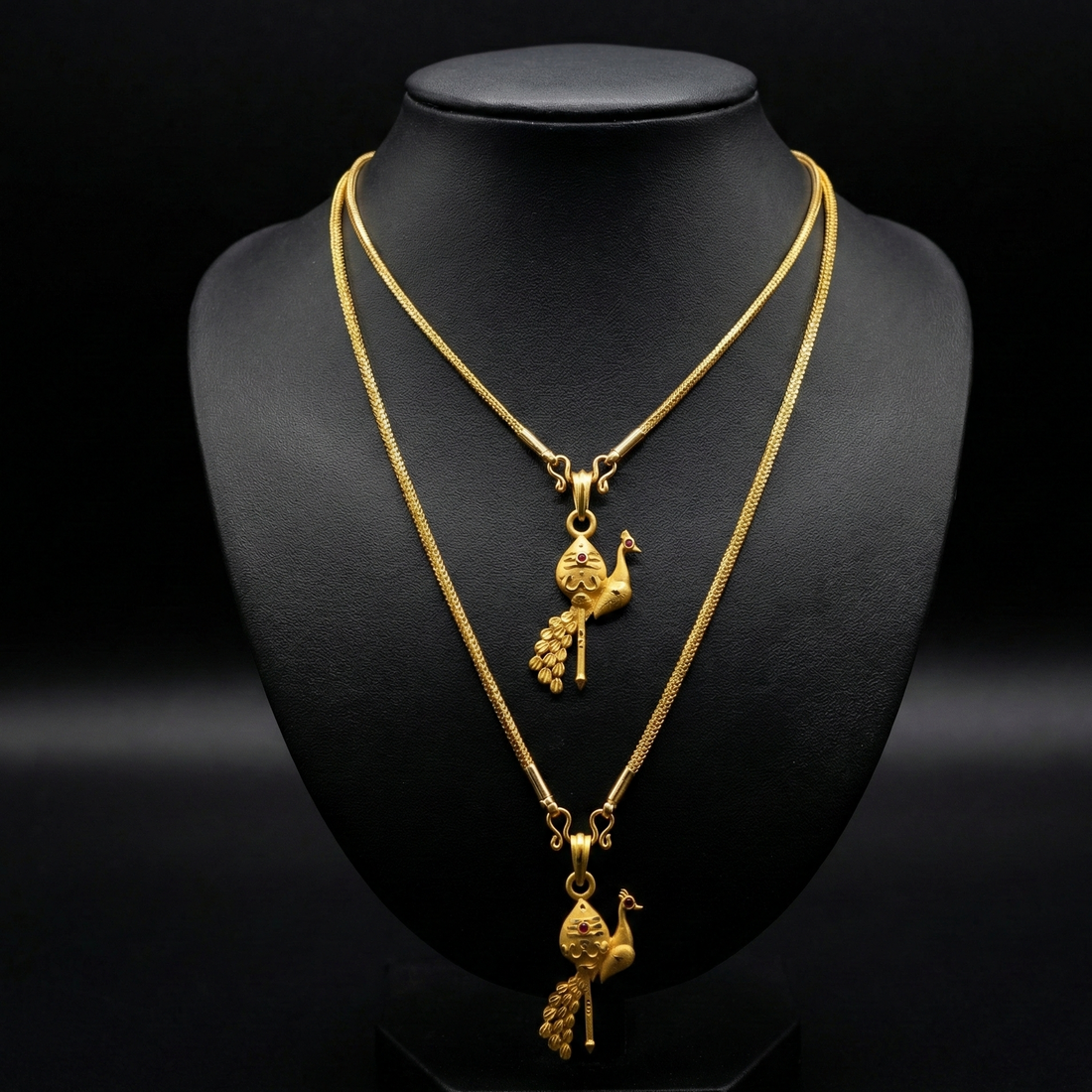 Two gold necklaces with pendants on a black mannequin bust.