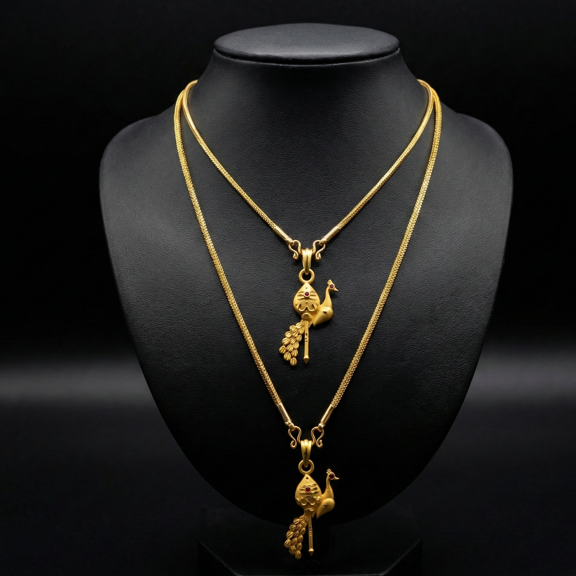 Two gold necklaces with pendants on a black mannequin bust.