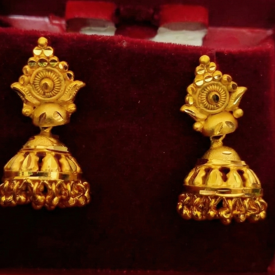 Gold earrings in a red box held by a hand with a blurred green background